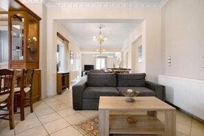 Een ruime woonkamer met een bank, een salontafel en een eethoek met stoelen en een kast.