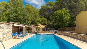 A swimming pool with lounge chairs, a stone building, and a fenced area with trees.