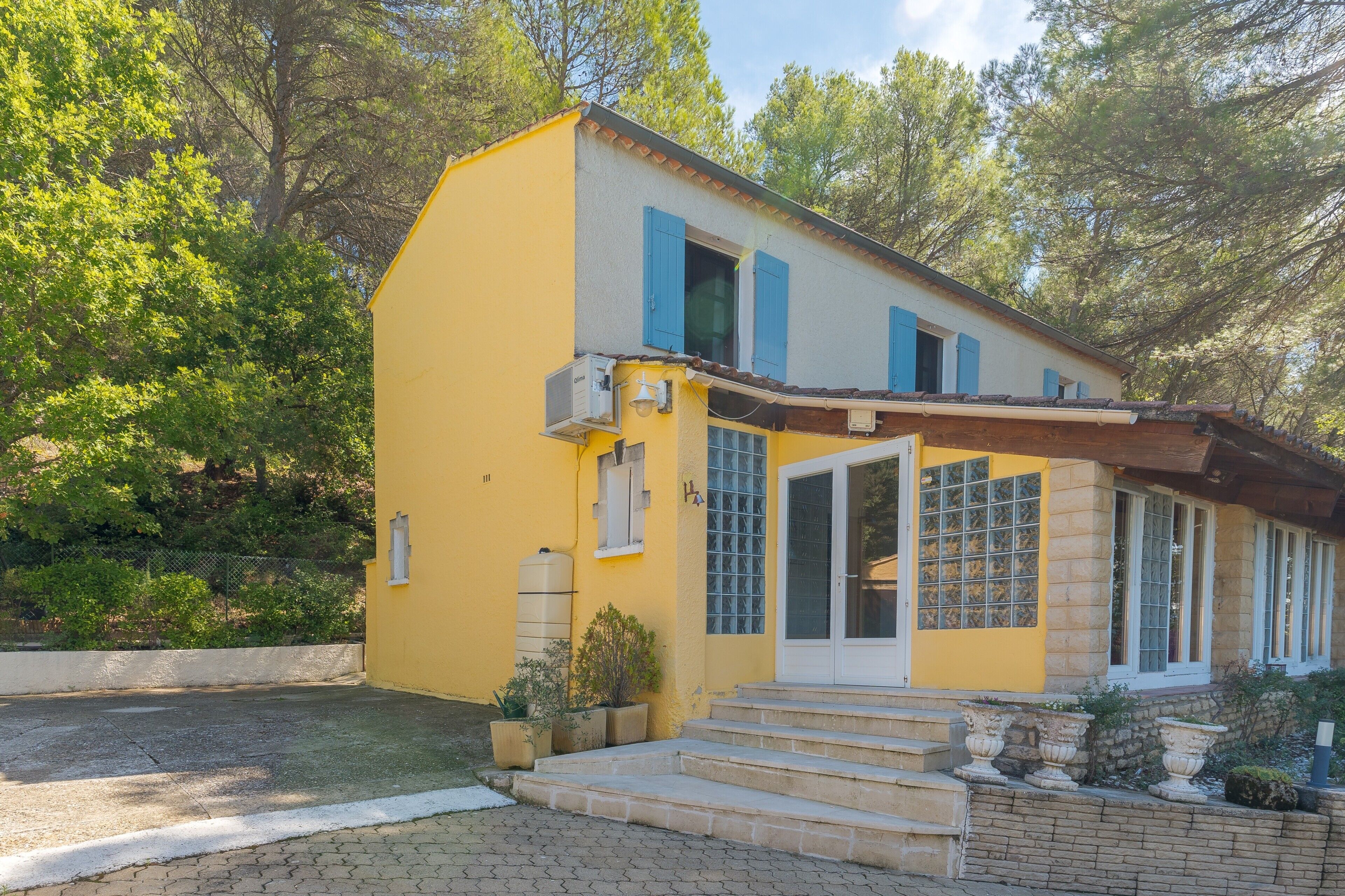 Un bâtiment jaune avec des volets bleus, une porte d’entrée et des marches menant à l’entrée.