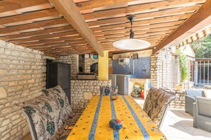 A covered outdoor dining area with stone walls, a wooden ceiling, and a table with a yellow tablecloth.