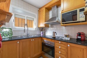 Une cuisine avec des meubles de rangement en bois, un évier en acier inoxydable, un four à micro-ondes et une machine à café rouge.
