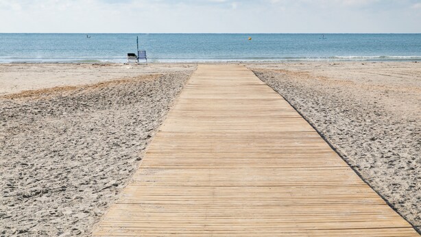 Une promenade en bois menant à une plage, avec un banc et un poste de surveillance pour les sauveteurs.