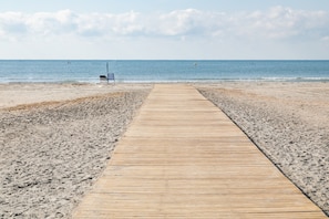 Une promenade en bois menant à une plage, avec un banc et un poste de surveillance pour les sauveteurs.