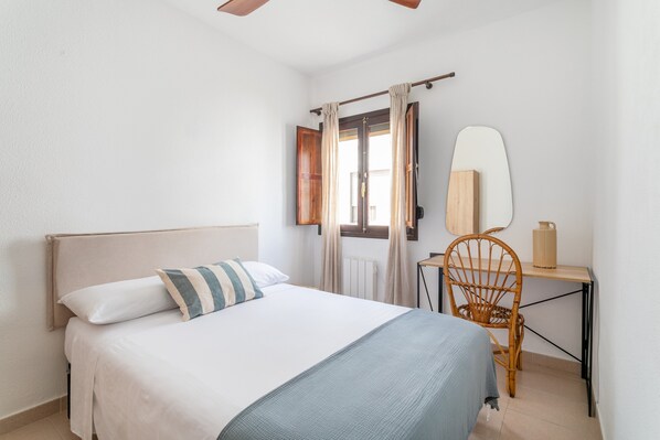 A bedroom with a bed, a chair, a desk, and a window with curtains.