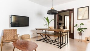 Un salon moderne avec une table à manger en bois, un canapé, un téléviseur et un luminaire suspendu.