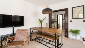 Un coin repas avec une table en bois, un banc en métal et un téléviseur fixé au mur.