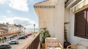 Un balcon avec des fauteuils en osier, une plante en pot et une vue sur la plage et la rue.