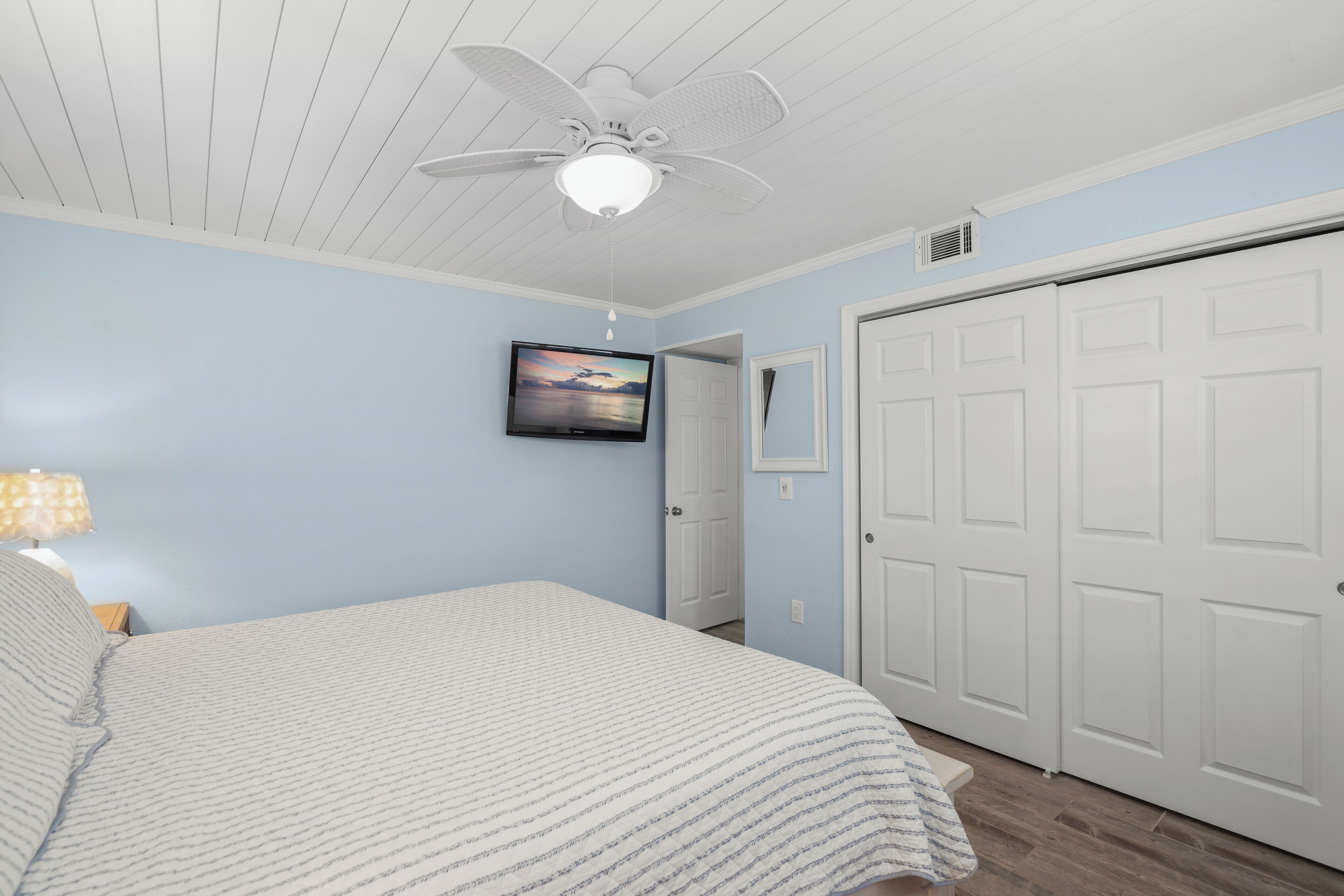 Un dormitorio con cama, ventilador de techo, televisor y armario.