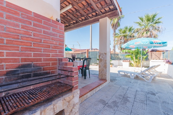 A brick barbecue grill, outdoor seating with chairs, a table, and a blue umbrella.