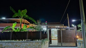 A gated property with a stone wall, a wooden fence, and a house with a tiled roof.