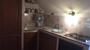 A kitchen with wooden cabinets, a gas stove, a fan, and a tiled backsplash. - Apartment 'Residence Lithos' with Mountain View, Garden and Wi-Fi (Petralia Soprana)