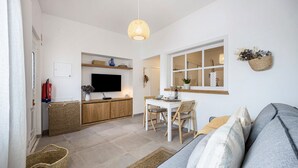 Ein modernes Wohnzimmer mit Sofa, Esstisch mit Stühlen, Fernseher und Küchenzeile mit Arbeitsfläche und Schränken.