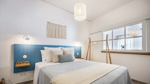Ein Schlafzimmer mit Bett, Nachttischen, einem Wandregal, einem Fenster mit Vorhängen und einer Pendelleuchte.