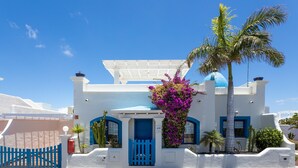 Un bâtiment blanc agrémenté de touches de bleu, une porte bleue et un palmier.