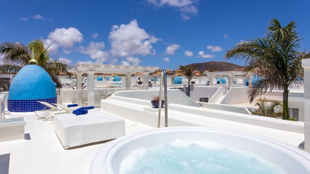 Un espace piscine aménagé sur le toit, avec un jacuzzi, des chaises longues et une vue sur les bâtiments environnants.