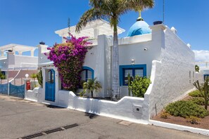 Un bâtiment blanc agrémenté de touches de bleu, surmonté d’un dôme bleu et orné d’une plante à fleurs roses.