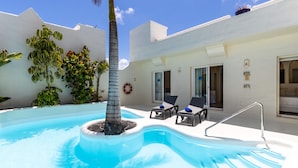 Une piscine avec un palmier, des chaises longues et un bâtiment blanc doté d’une porte et de fenêtres.
