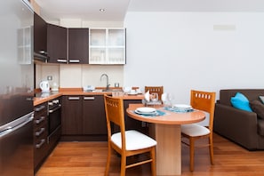 Une cuisine moderne avec des meubles de couleur sombre, un four encastré et un coin repas comprenant une table et des chaises en bois.