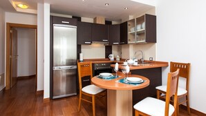A compact kitchen with a central island, wooden chairs, a refrigerator, and cabinets. - Vacation Home "Corralejo Main Street" with Terrace & Wi-Fi (Corralejo)