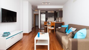 A modern living room with a sofa, a coffee table, a TV, and a kitchen in the background. - Vacation Home "Corralejo Main Street" with Terrace & Wi-Fi (Corralejo)