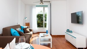A modern living room with a sofa, coffee table, TV, and a window with curtains. - Vacation Home "Corralejo Main Street" with Terrace & Wi-Fi (Corralejo)
