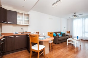 A modern kitchen with wooden cabinets, a dining table with chairs, a sofa, and a ceiling fan.