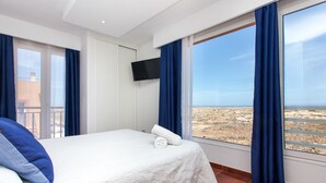 Una habitación de hotel con una cama, televisión y un ventanal con cortinas.