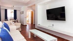 Un salón moderno con un televisor de pantalla plana, una mesa de centro de vidrio y un sofá con cojines azules.