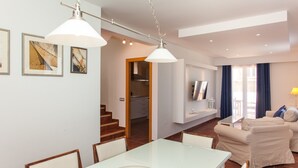 Una sala de estar moderna con comedor, un conjunto de sofás y una cocina al fondo.