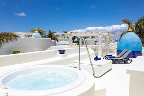 Un bain à remous avec un espace aménagé au bord de la piscine, des chaises longues et une pergola dotée de parasols.