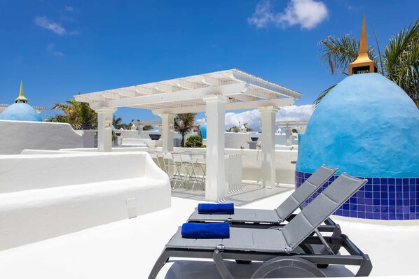 Un espace piscine aménagé sur le toit, avec des chaises longues, une pergola et des structures surmontées de dômes bleus.