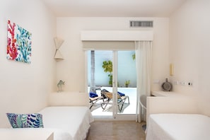 A hotel room with two beds, a large sliding glass door to a balcony, a ceiling vent, and a wall-mounted lamp.