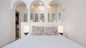 A bedroom with a large bed, two bedside lamps, and a wardrobe with glass doors.
