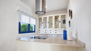 A kitchen with a central island, white cabinetry, a stainless steel range hood, and a window with a view of greenery.