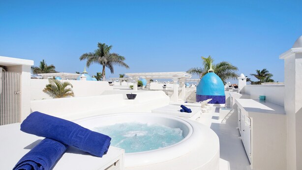 A rooftop with a hot tub, white walls, blue accents, and palm trees.