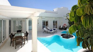 A modern outdoor pool area with lounge chairs, a dining table, and a small garden.