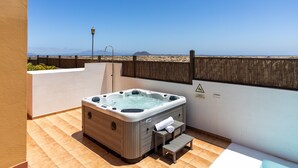 A hot tub on a balcony with a view of the beach and mountains.