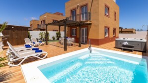 A pool area with lounge chairs, a hot tub, and a covered patio.