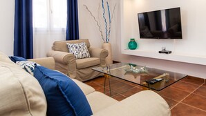A modern living room with a sofa, a glass coffee table, a flat-screen TV mounted on the wall, and a decorative vase.