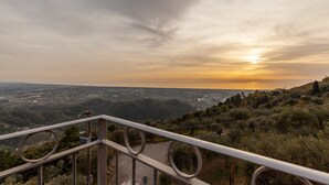 Una vista panorámica desde un punto elevado, con barandilla de metal, sobre un valle con el atardecer al fondo.