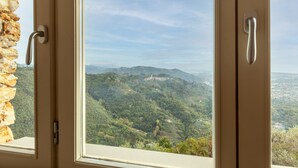 Una ventana con vistas a un paisaje montañoso, un muro de piedra y una puerta con pomo.