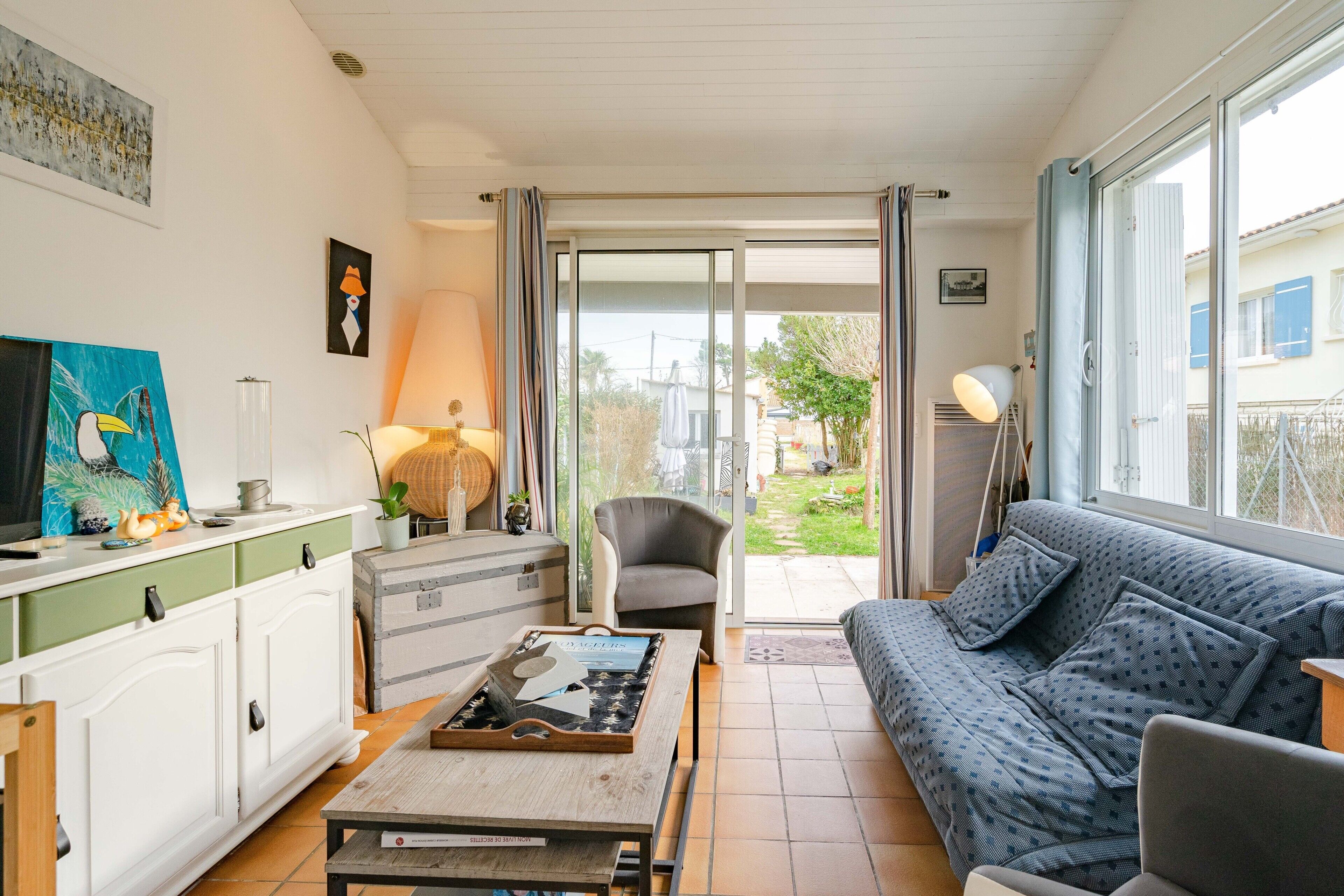 A living room with a sofa, a table, a chair, and a sliding glass door leading to a garden.