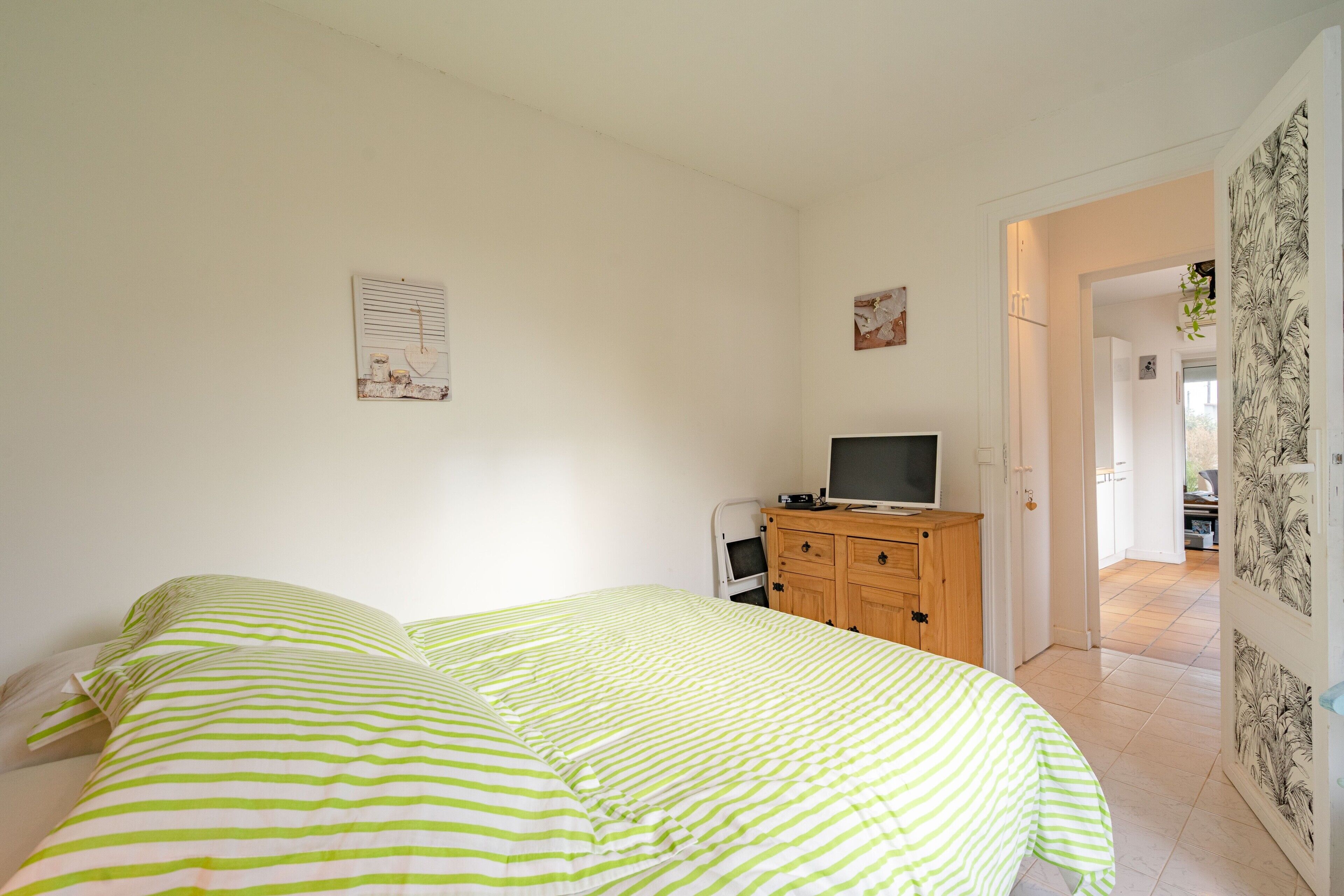Een slaapkamer met een bed, een televisie, een houten dressoir en een deur naar een andere kamer.