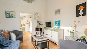 Ett vardagsrum med en soffa, fåtölj, soffbord, TV, skåp och konstverk på väggarna.