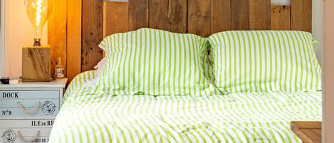 Una cama con ropa de cama verde y blanca a rayas, un cabecero de madera y una mesita de noche con lámpara y adornos.