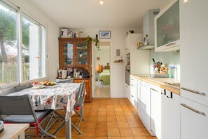 A compact kitchen with a dining area, a cabinet with glass doors, and a view through an open door to a bedroom.