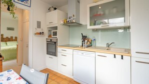 Ett kompakt kök med vita skåp, diskmaskin, mikrovågsugn och en diskho med ett stänkskydd av glas.
