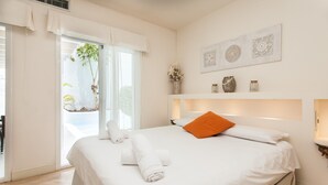 A hotel room with a bed, a window with curtains, a wall-mounted shelf with decorative items, and a door leading to an outdoor area. - Vacation Home "Villa 82" with Mountain View, Pool & Wi-Fi (Corralejo)