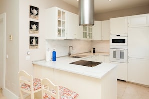 A modern kitchen with white cabinets, a stainless steel sink, a built-in oven, and a small island with chairs.