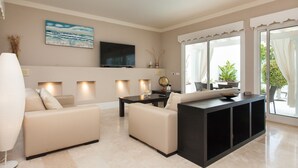 A modern living room with a sofa, a coffee table, a TV, and a large window with curtains. - Vacation Home "Villa 82" with Mountain View, Pool & Wi-Fi (Corralejo)